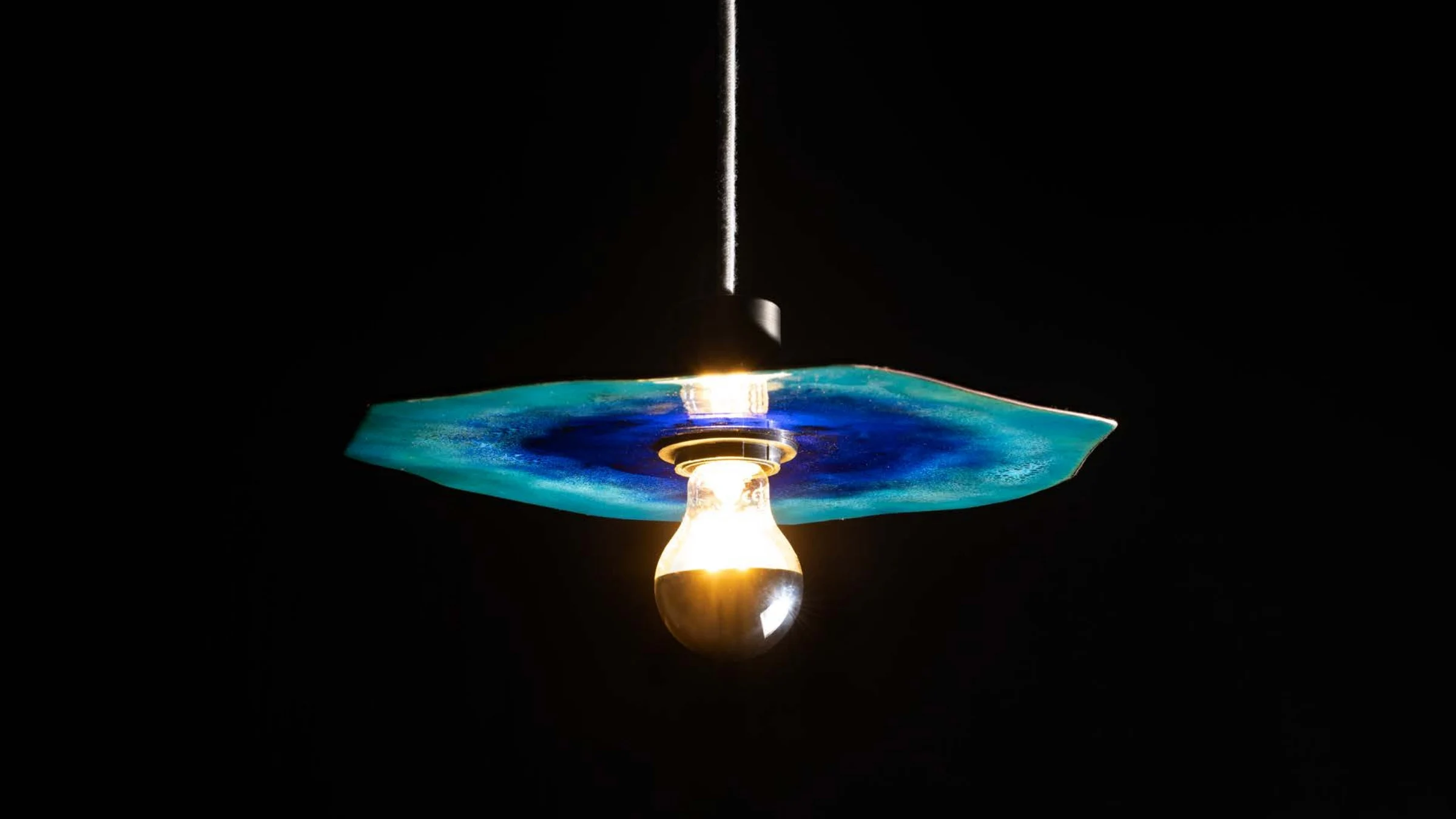 Suspension en émail bleu éclairée sur un fond noir profond