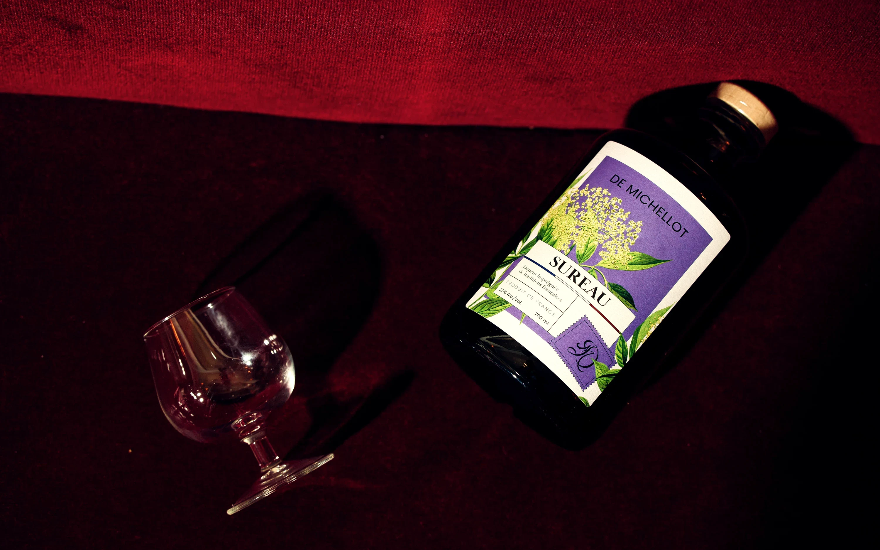 Bouteille de liqueur de sureau De Michellot et verre vintage sur un velours bordeaux, photographie du shooting original
