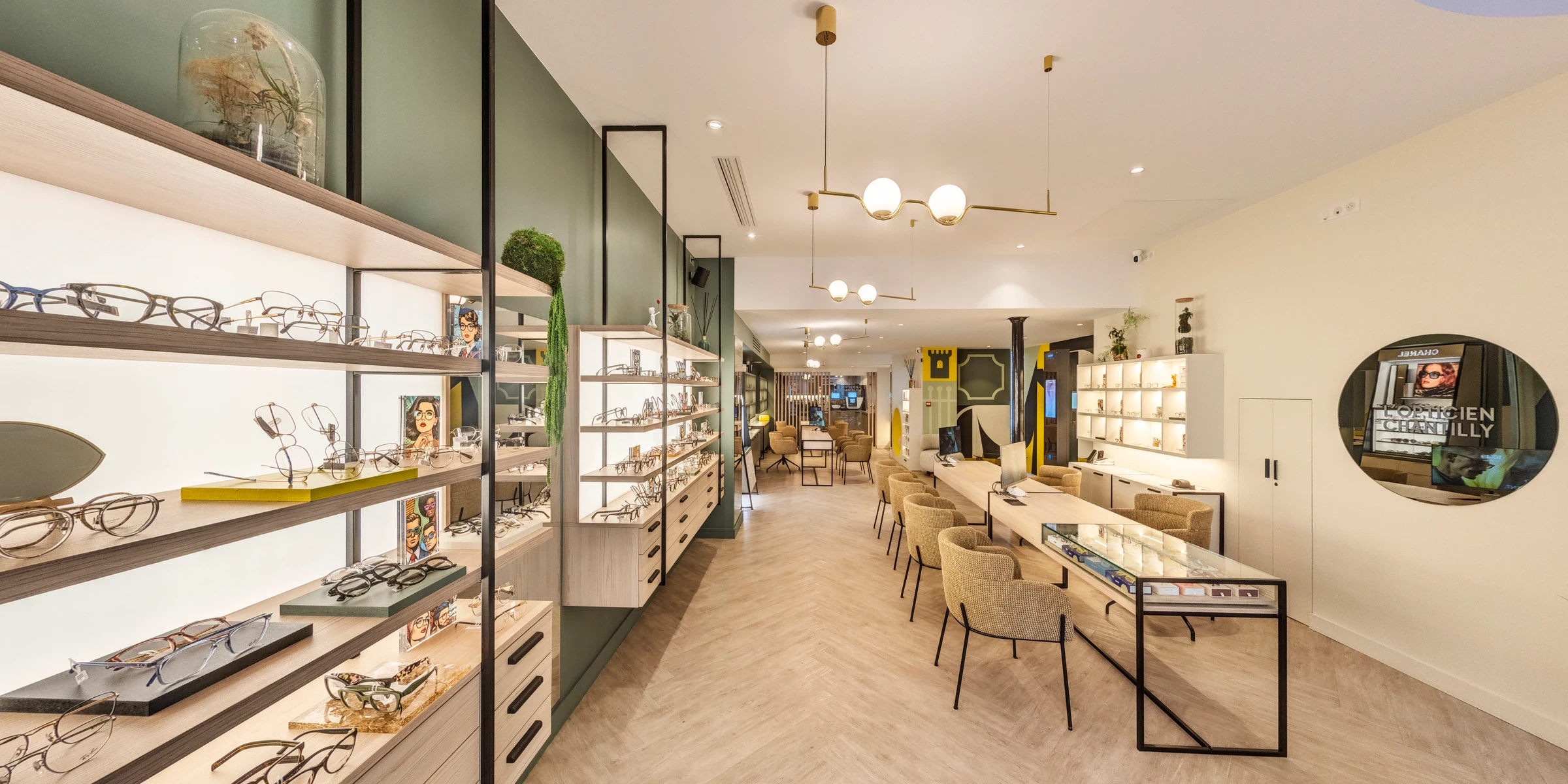 Intérieur de L’Opticien de Chantilly, mobilier vert, parquet, suspensions en forme de lunettes et miroir portant le logotype