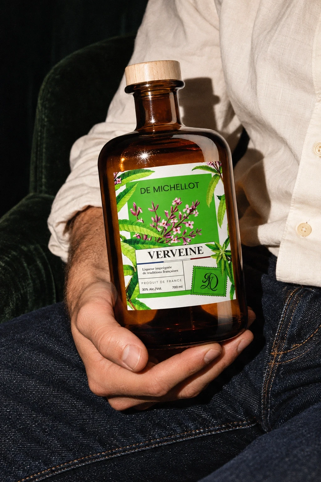 Flacon Verveine De Michellot tenu en main contre une chemise en lin et un jean, lumière au flash et grain — scène générée
