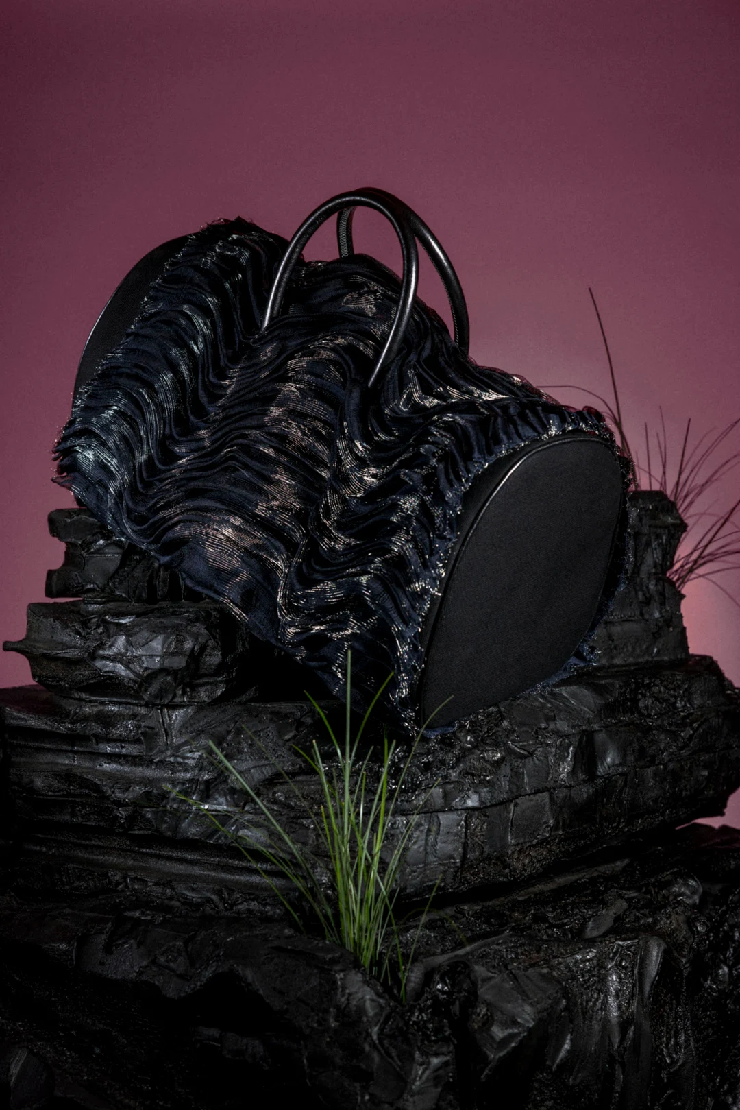 Sac noir aux plis métalliques posé sur un relief minéral sombre