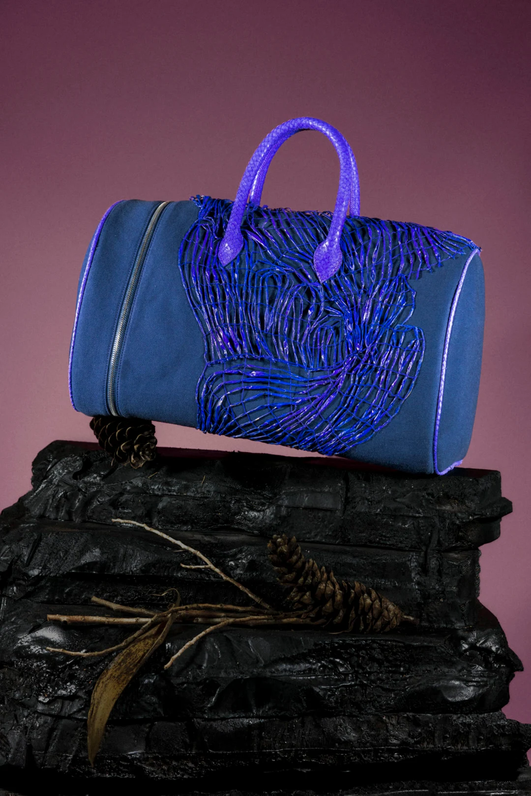 Sac bleu et violet texturé posé sur un socle minéral noir