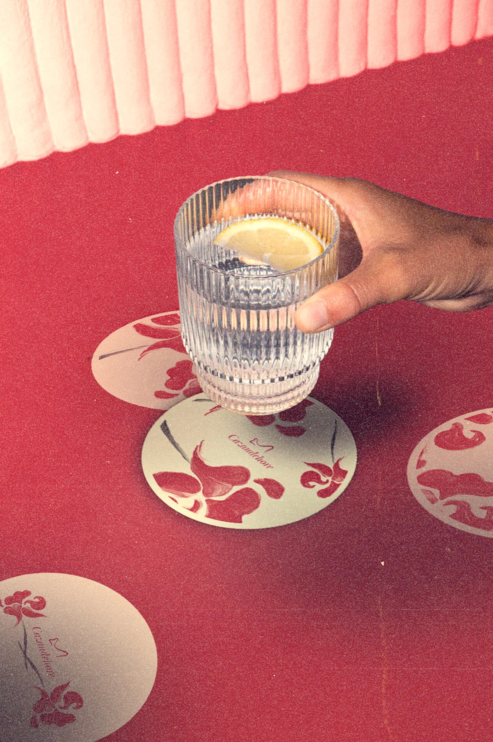 Sous-bocks Cazaudehore au motif floral rouge, mis en scène sur une table rouge avec un verre