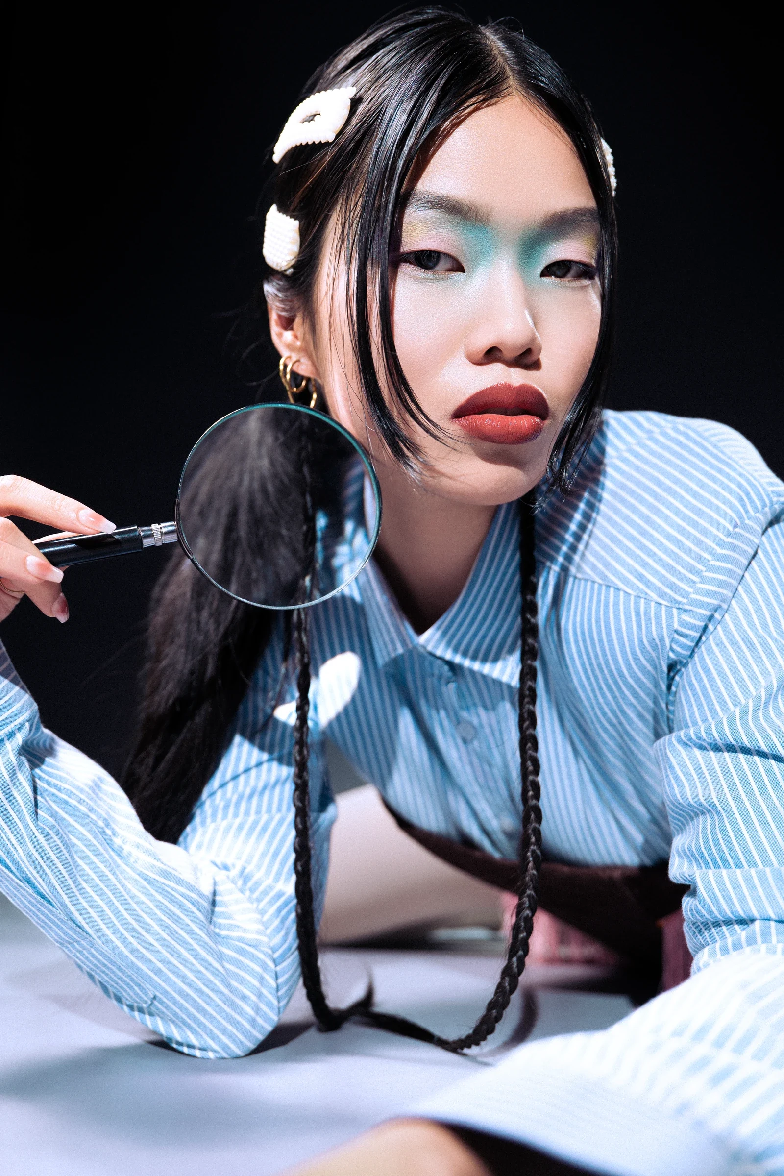 Portrait en chemise rayée bleue avec des accessoires dans les cheveux et une loupe tenue près du visage