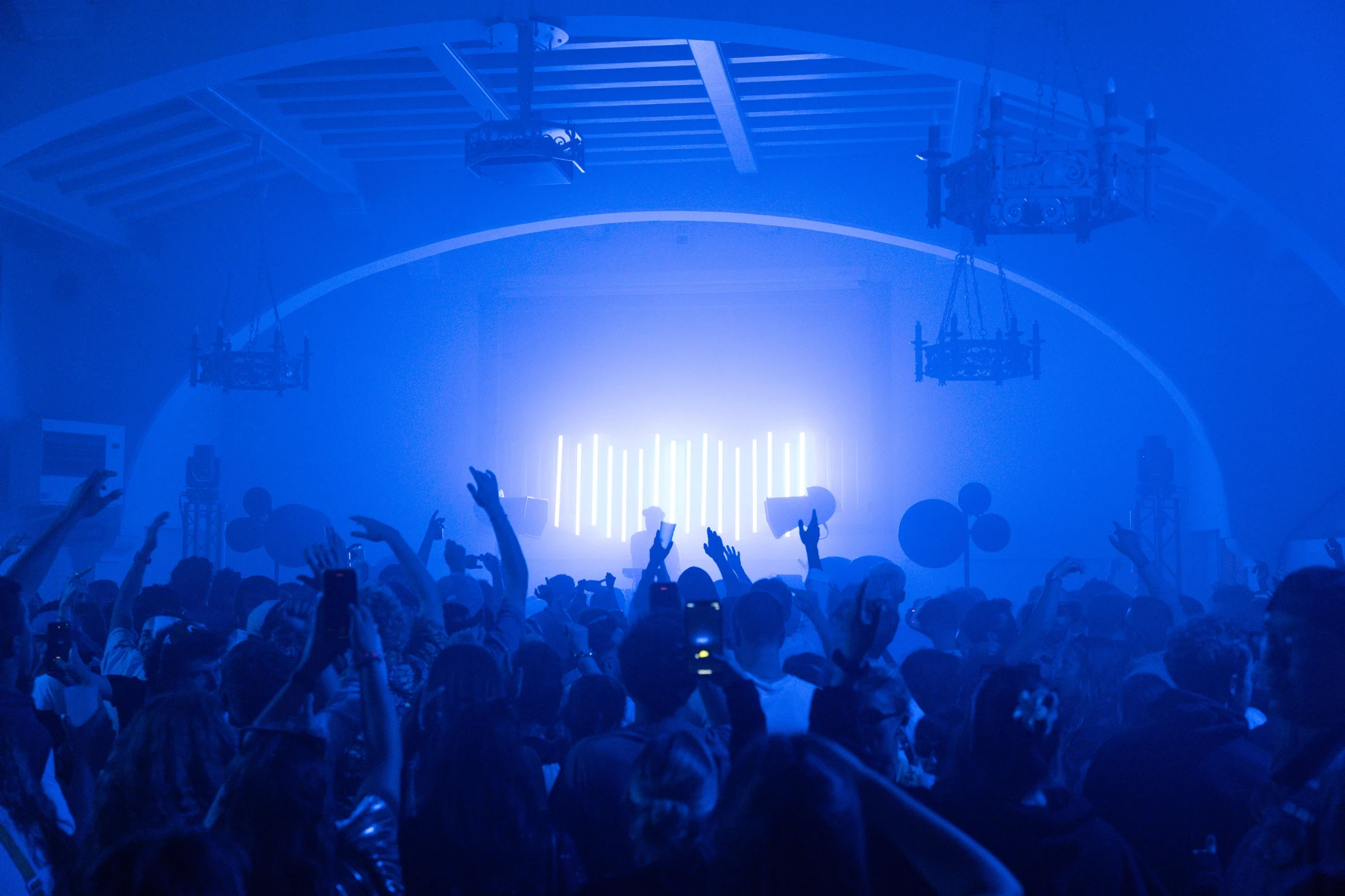 Public réuni sous une structure éclairée en bleu, bras levés face à la scène — Gärten on the Beach, première édition 2025. Photographie de Tom Radday.