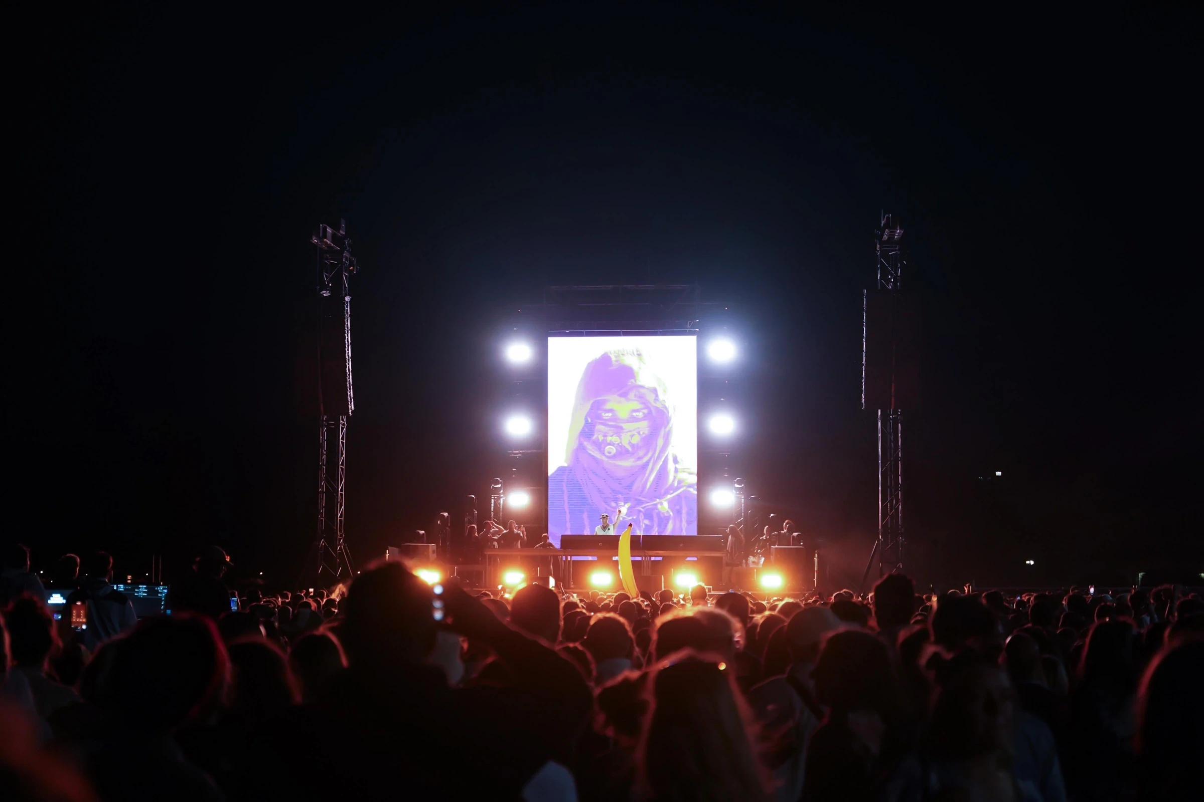 Vue nocturne de la scène extérieure avec écran vertical, projecteurs et public au premier plan — Gärten on the Beach, première édition 2025. Photographie de Tom Radday.