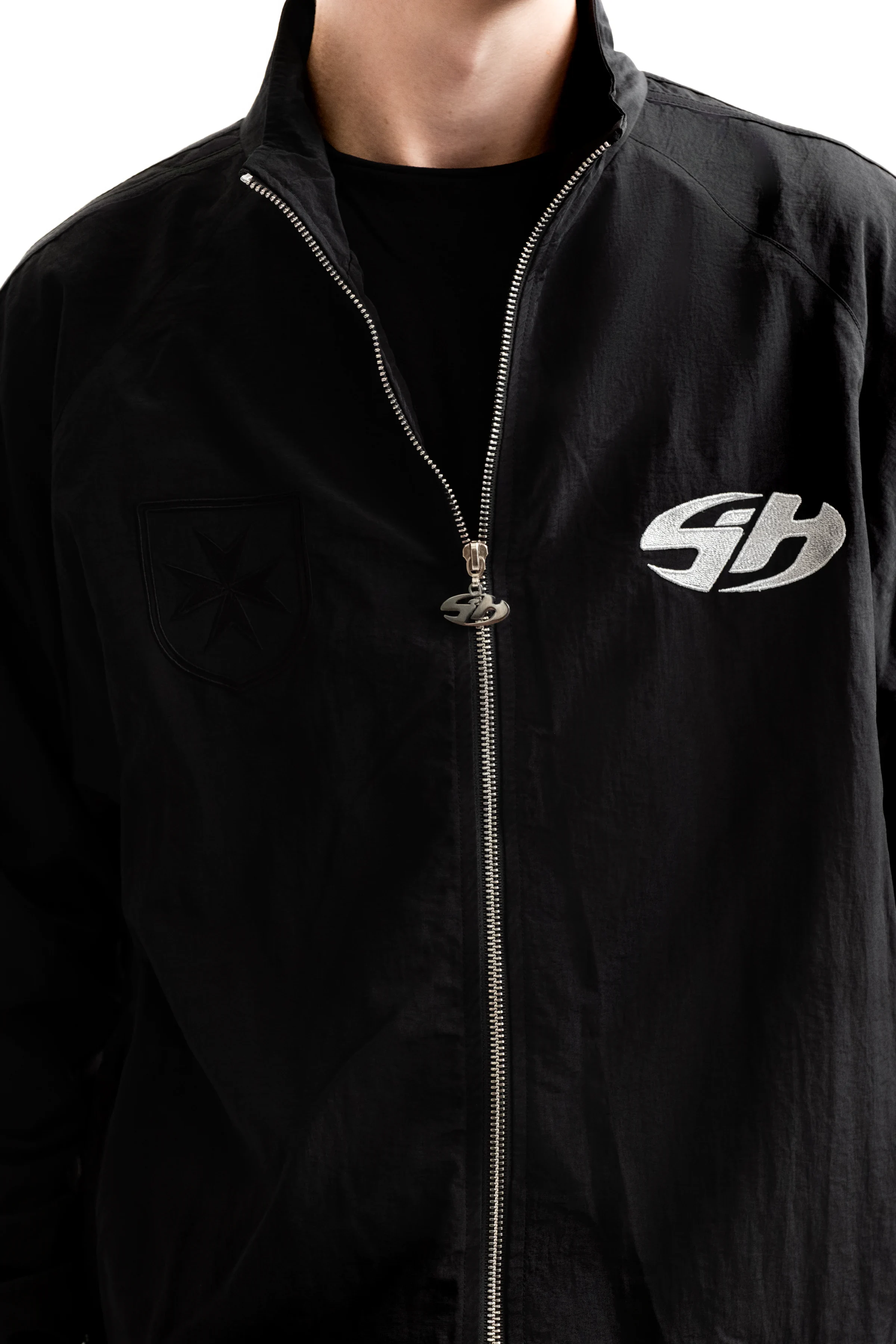 Gros plan porté d’une veste noire Sixty House montrant la broderie blanche, la tirette métallique et la matière du vêtement
