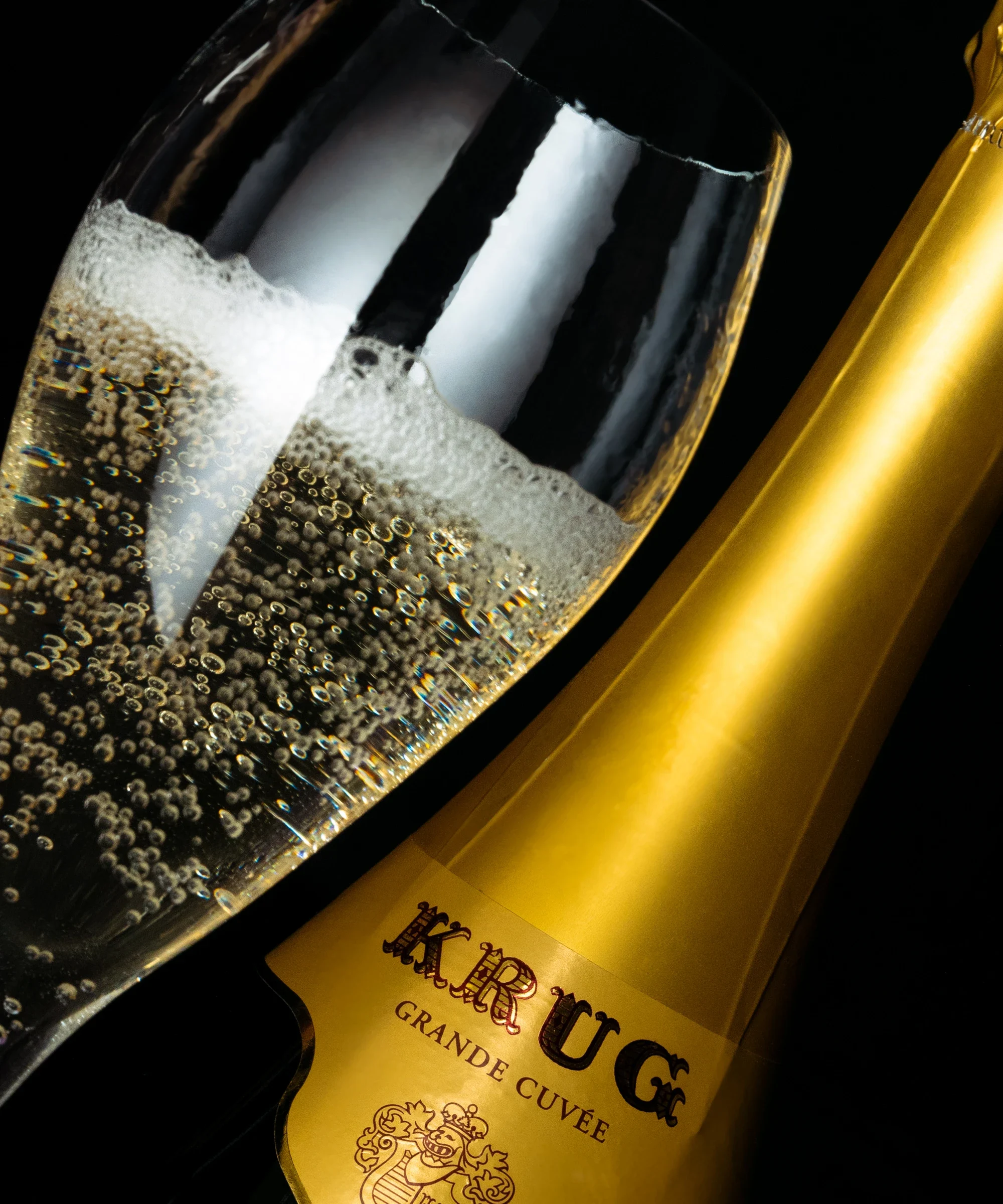 Gros plan oblique sur une flûte de champagne et une bouteille Krug Grande Cuvée, sur fond noir
