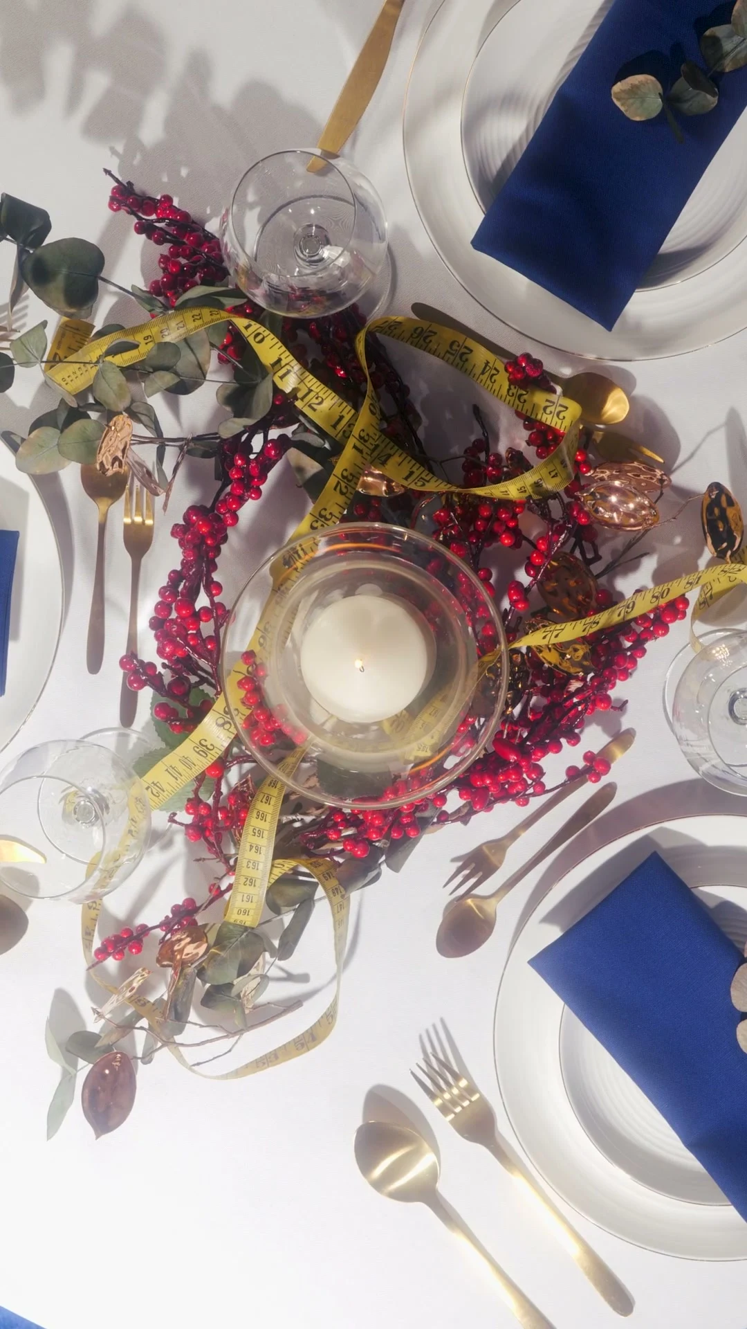 Table de fête vue du dessus avec ruban de couturière, baies rouges, vaisselle blanche et serviettes bleu nuit