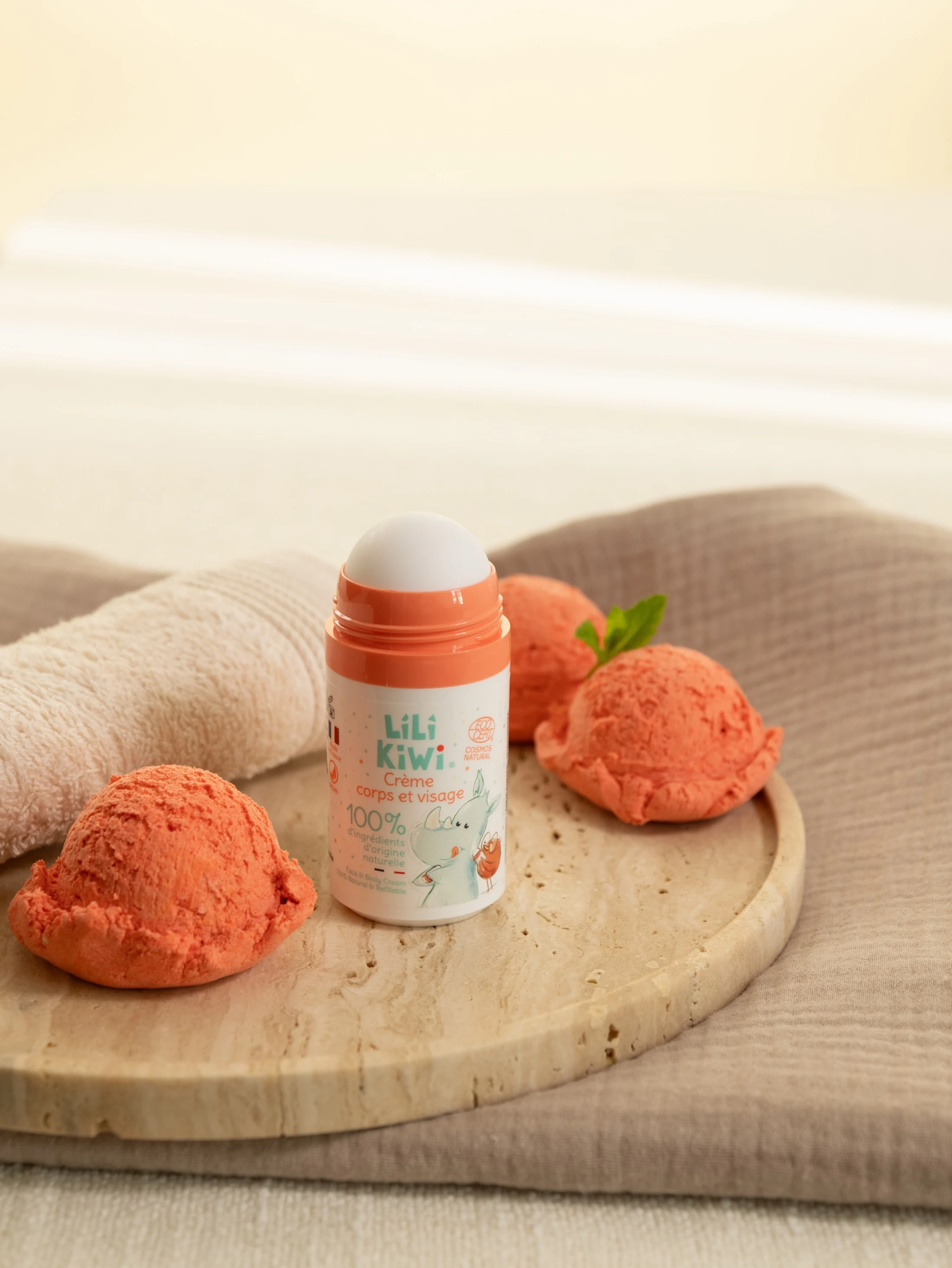 Crème corps et visage Lili Kiwi orange entourée de boules de sorbet pêche