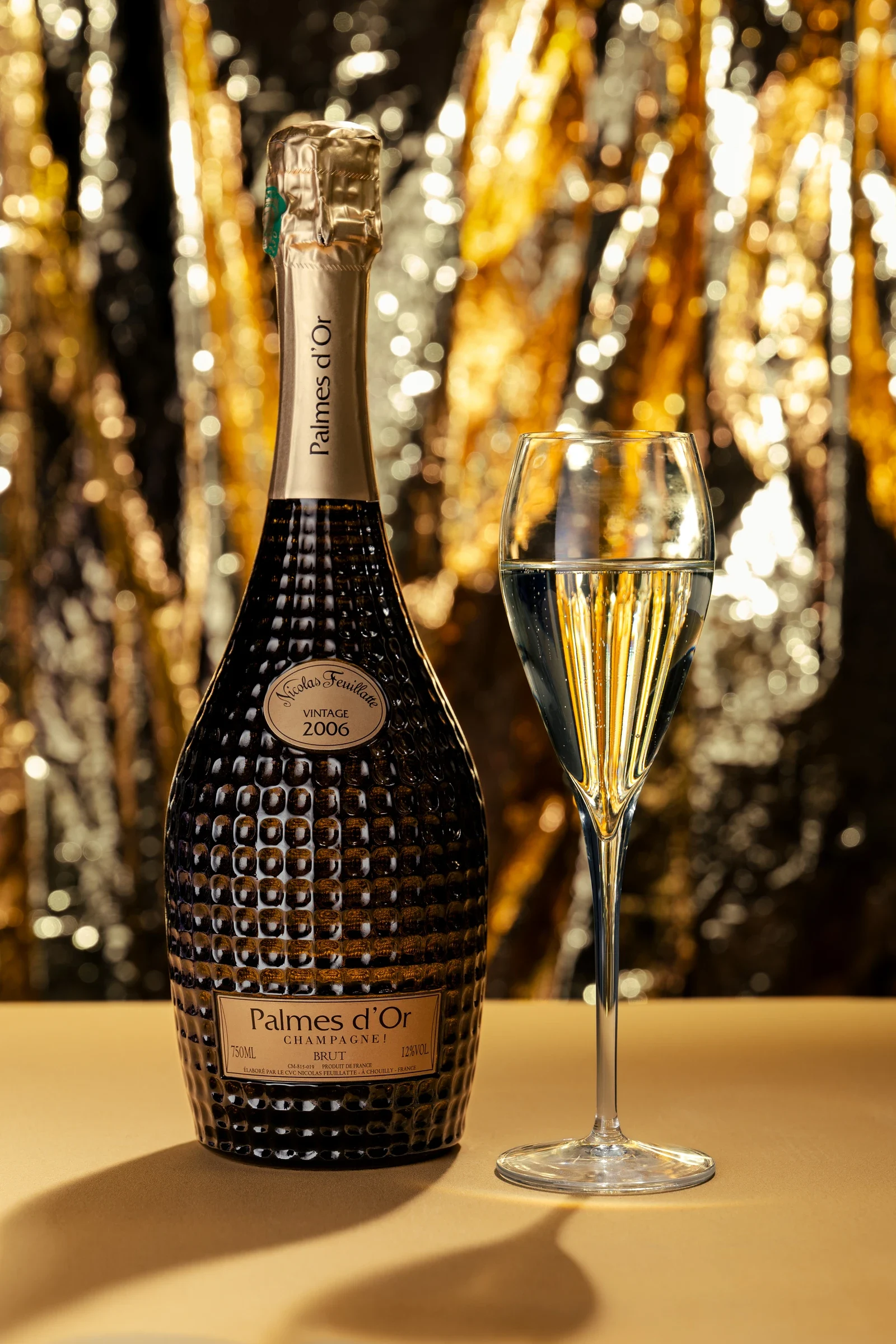 Bouteille Palmes d’Or Nicolas Feuillatte et flûte de champagne sur un fond de reflets dorés