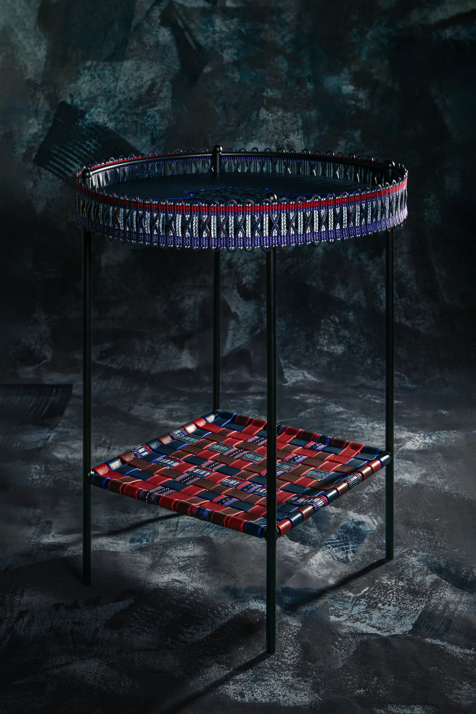 Table d’appoint Prémisse avec plateau bleu et cuir tressé rouge et bleu, photographiée sur un fond minéral sombre