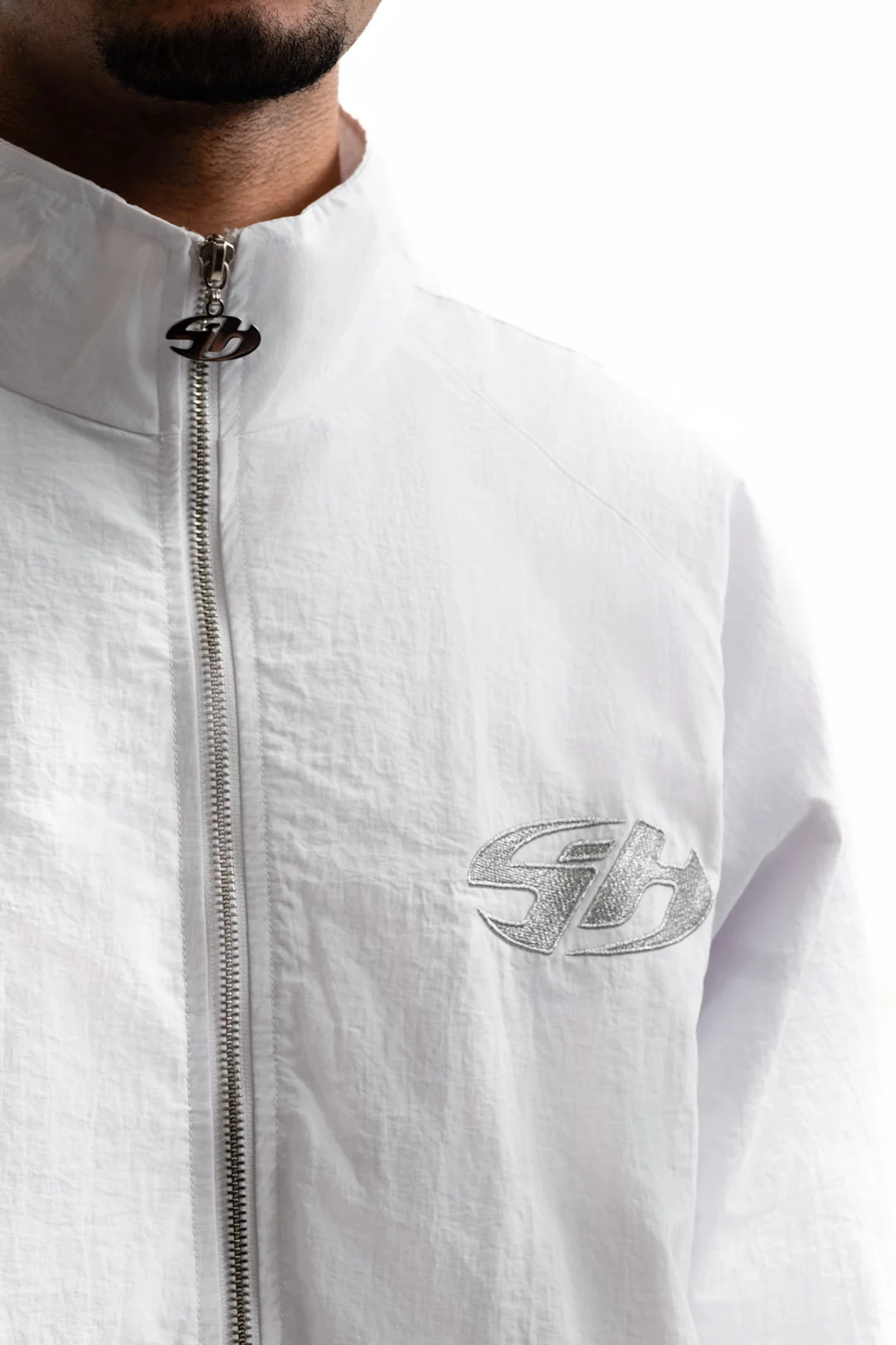 Détail d’une veste blanche Sixty House avec tirette monogrammée et broderie ton sur ton