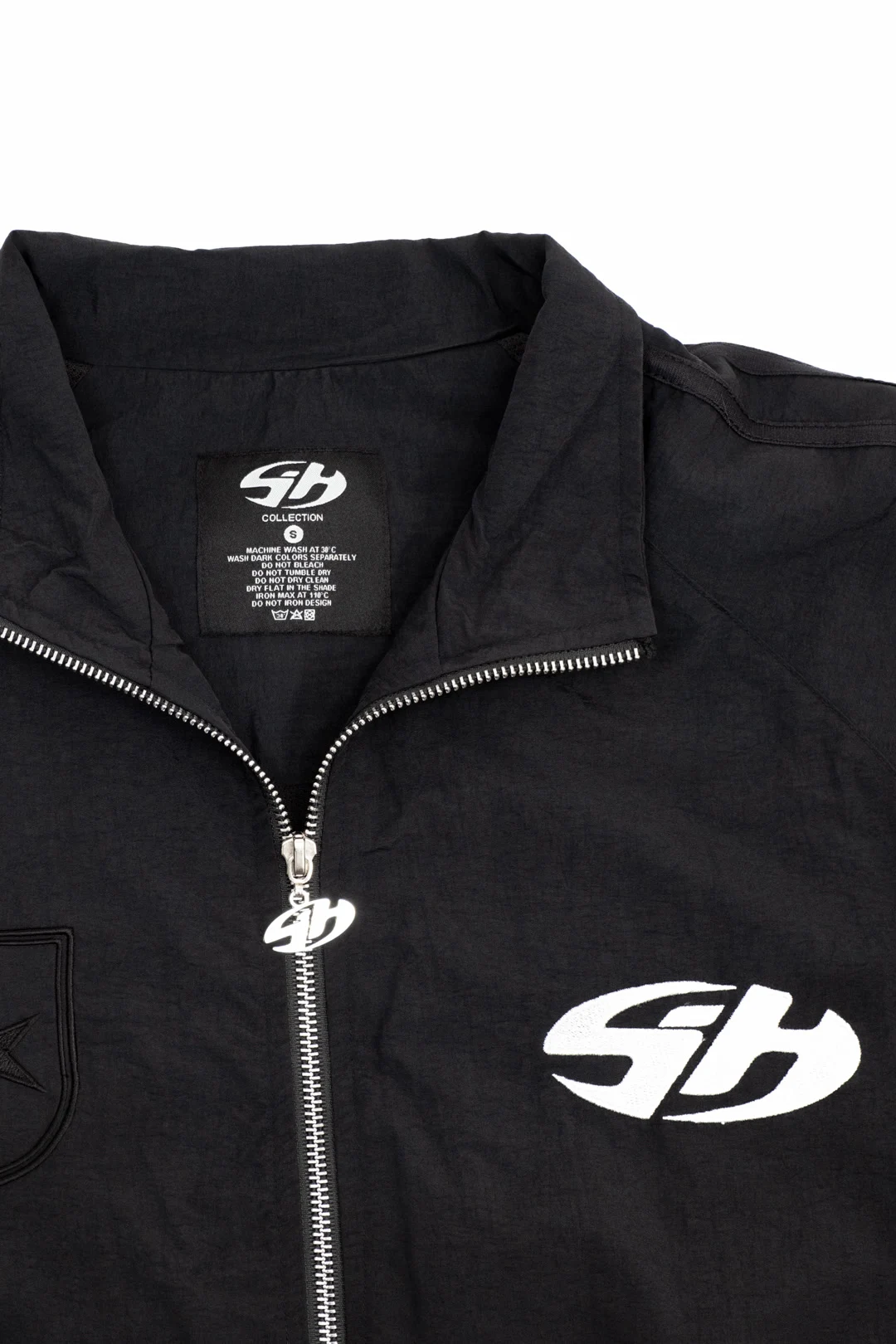 Gros plan sur la fermeture métallique et le monogramme blanc d’une veste noire Sixty House